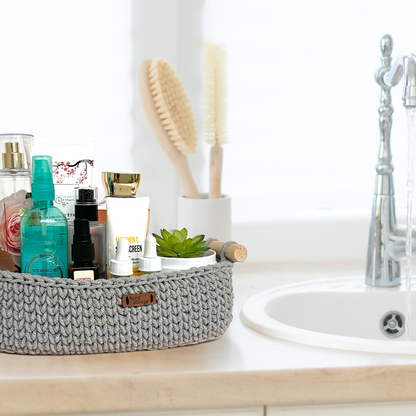 Bathroom counter with a gray woven basket containing skincare products, a small plant, and brushes.