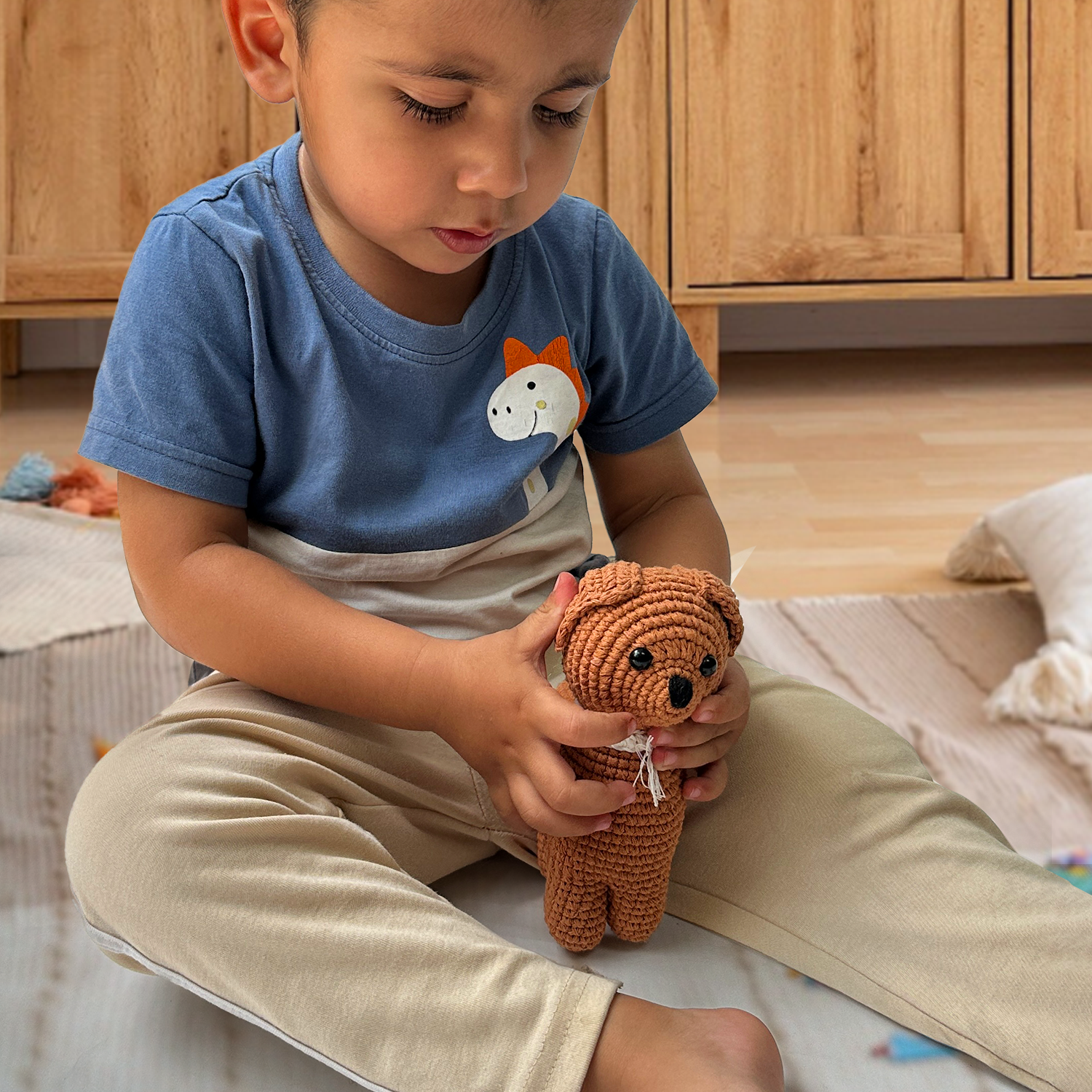 Child holding a brown teddy bear toy in a room with wooden cabinets.