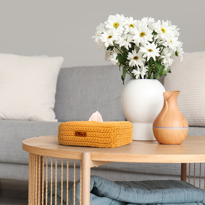 Coffee table with a vase of white flowers, wooden diffuser, and yellow tissue box in a living room setting.
