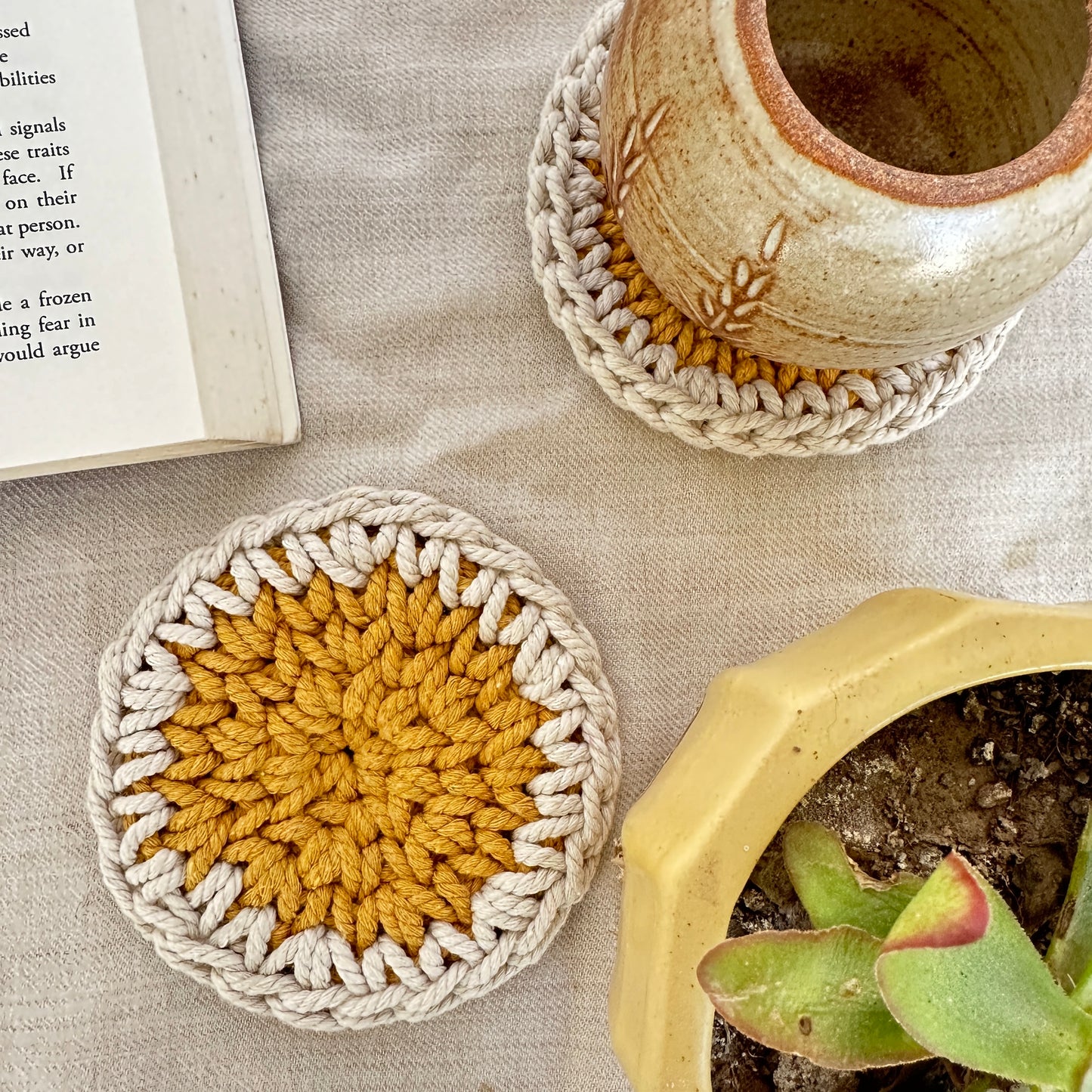 Crocheted coasters with a pot and book on a textured surface