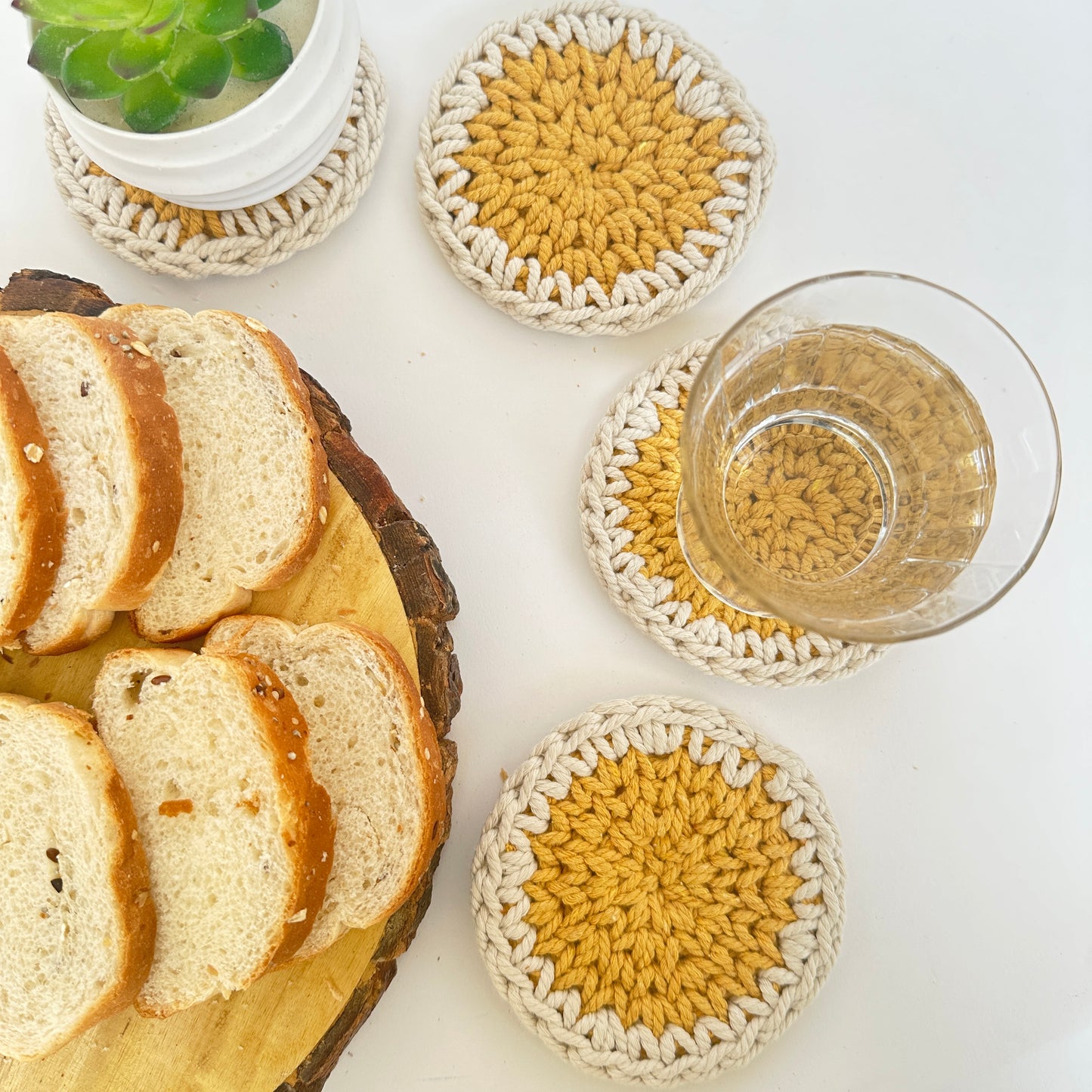 Crocheted coasters with bread and a glass of juice on a white surface