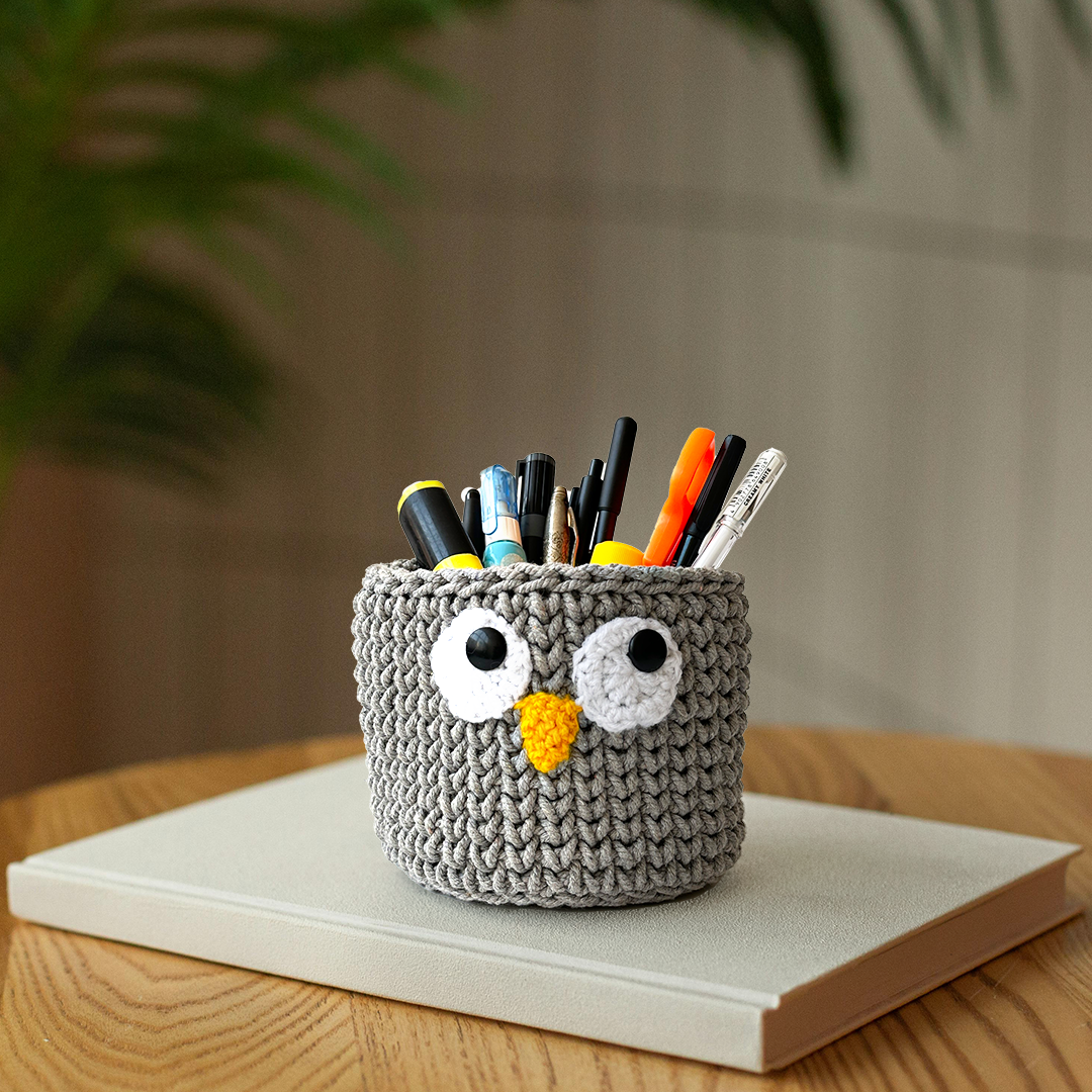 Crocheted owl-shaped pencil holder with pens on a wooden surface