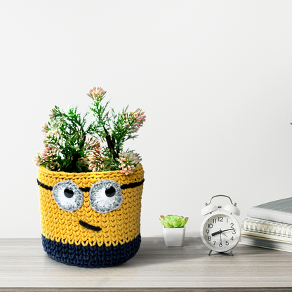 Crocheted pot shaped Basket  like a Minion with a plant on a desk.