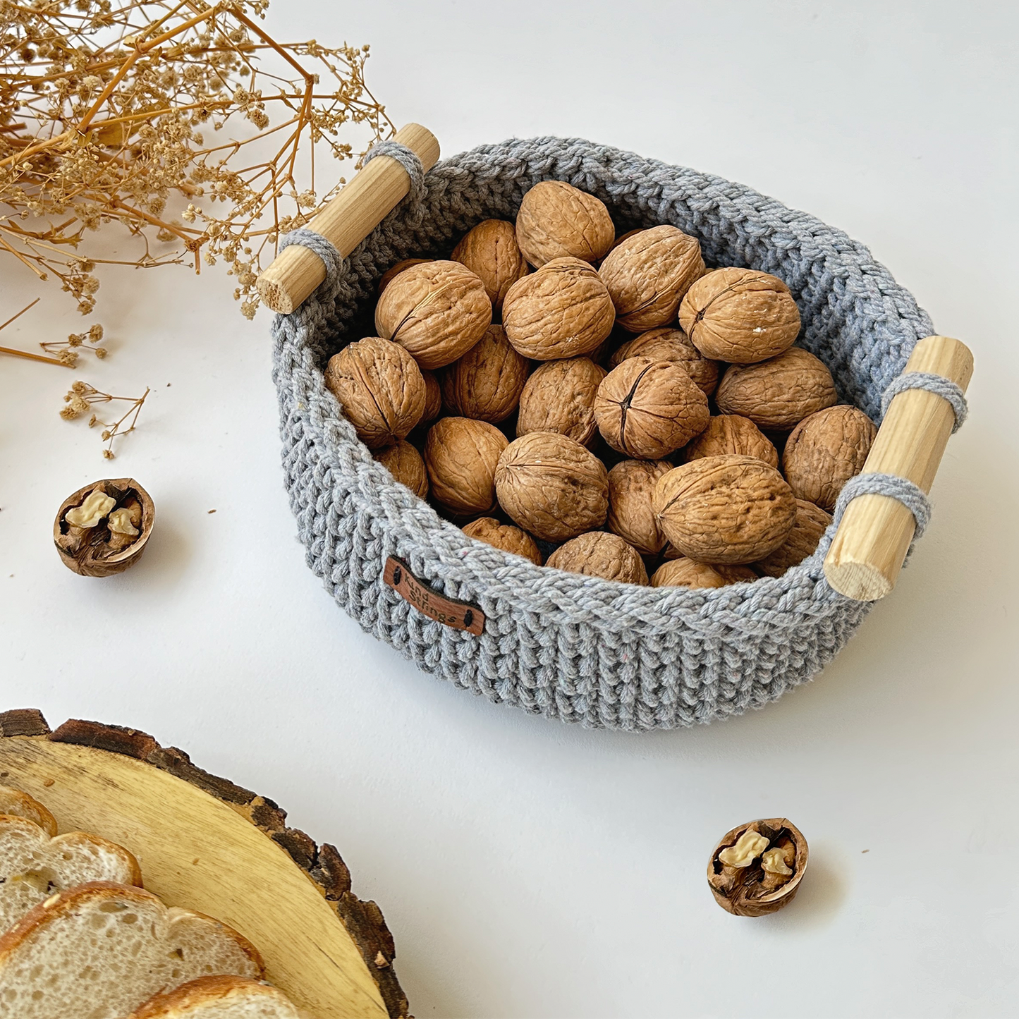 Gray woven basket with wooden handles filled with walnuts on a white surface.