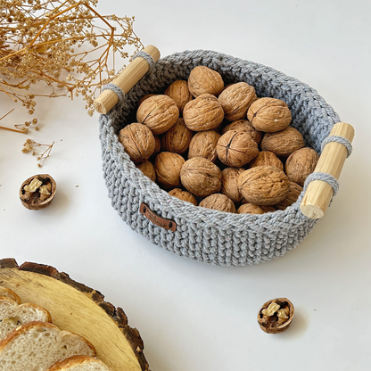 Gray woven basket with wooden handles filled with walnuts on a white surface.