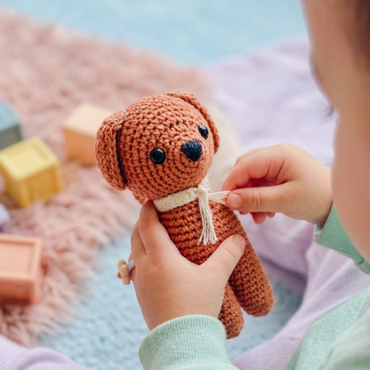 Hand holding a small brown knitted dog toy with colorful blocks in the background