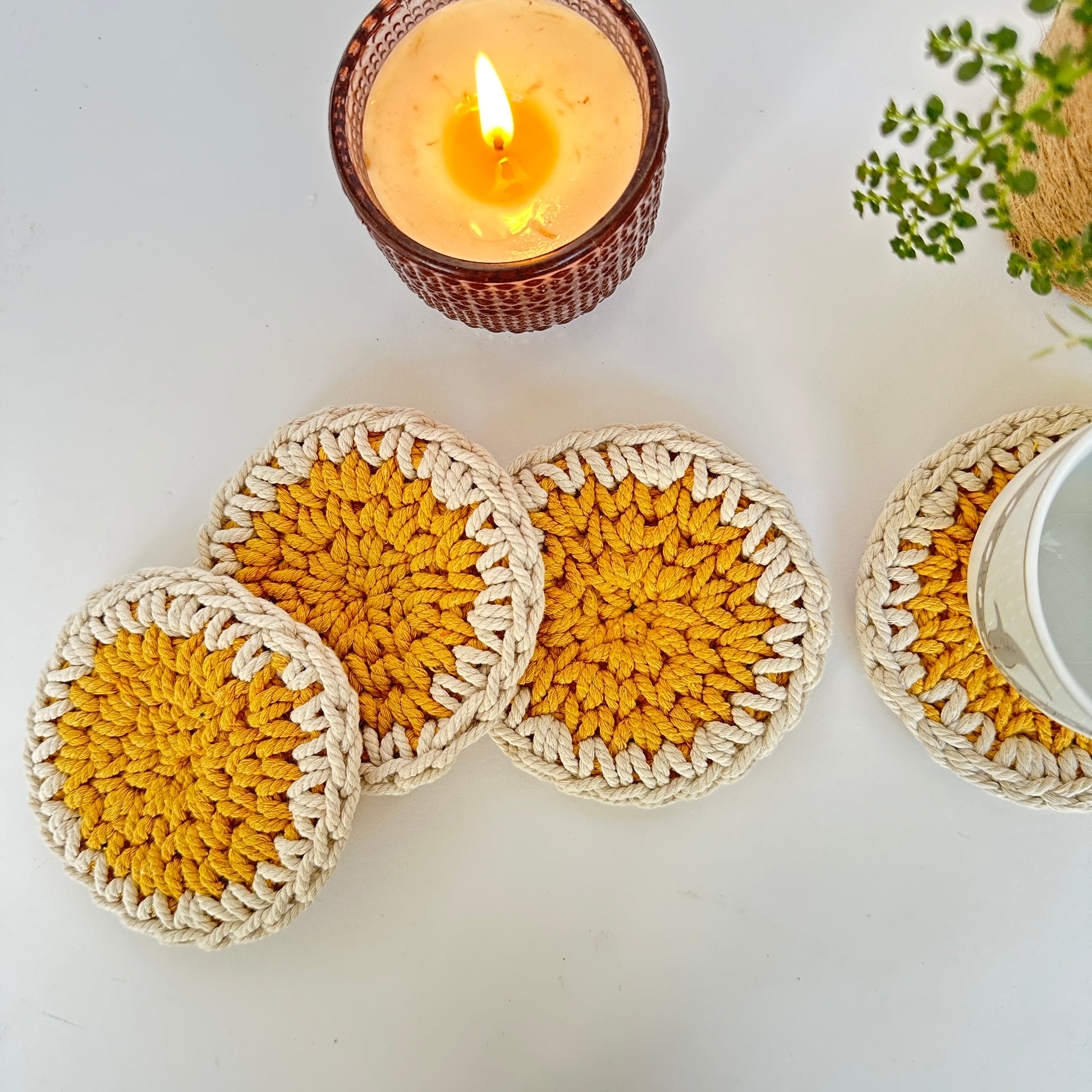 Set of crocheted coasters with a candle and plant in the background on a light surface.