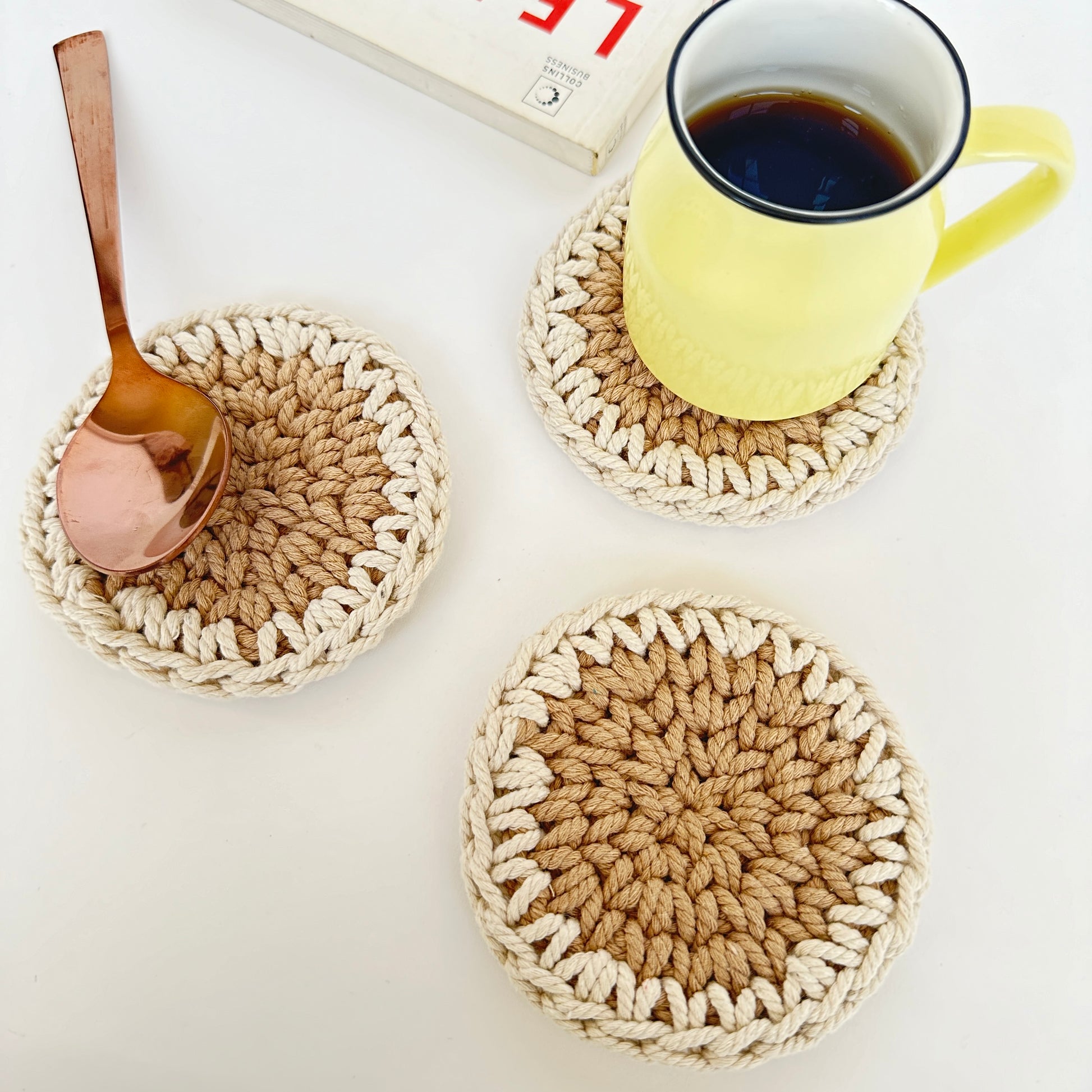 Three crocheted coasters with a mug of coffee and a spoon on a white surface.