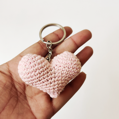 Pink heart-shaped keychain held in a hand against a white background