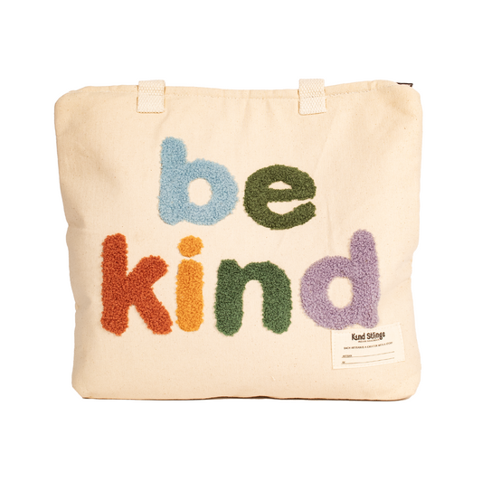 White tote bag with colorful 'be kind' text on a white background