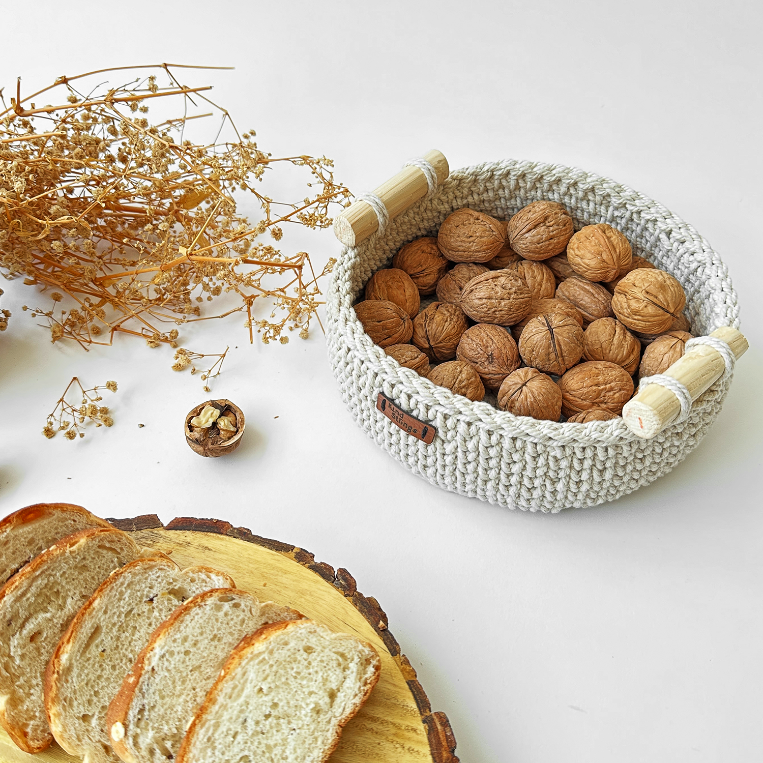 Woven basket with walnuts, sliced bread, and dried flowers on a white surface