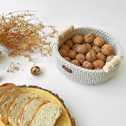 Woven basket with walnuts, sliced bread, and dried flowers on a white surface