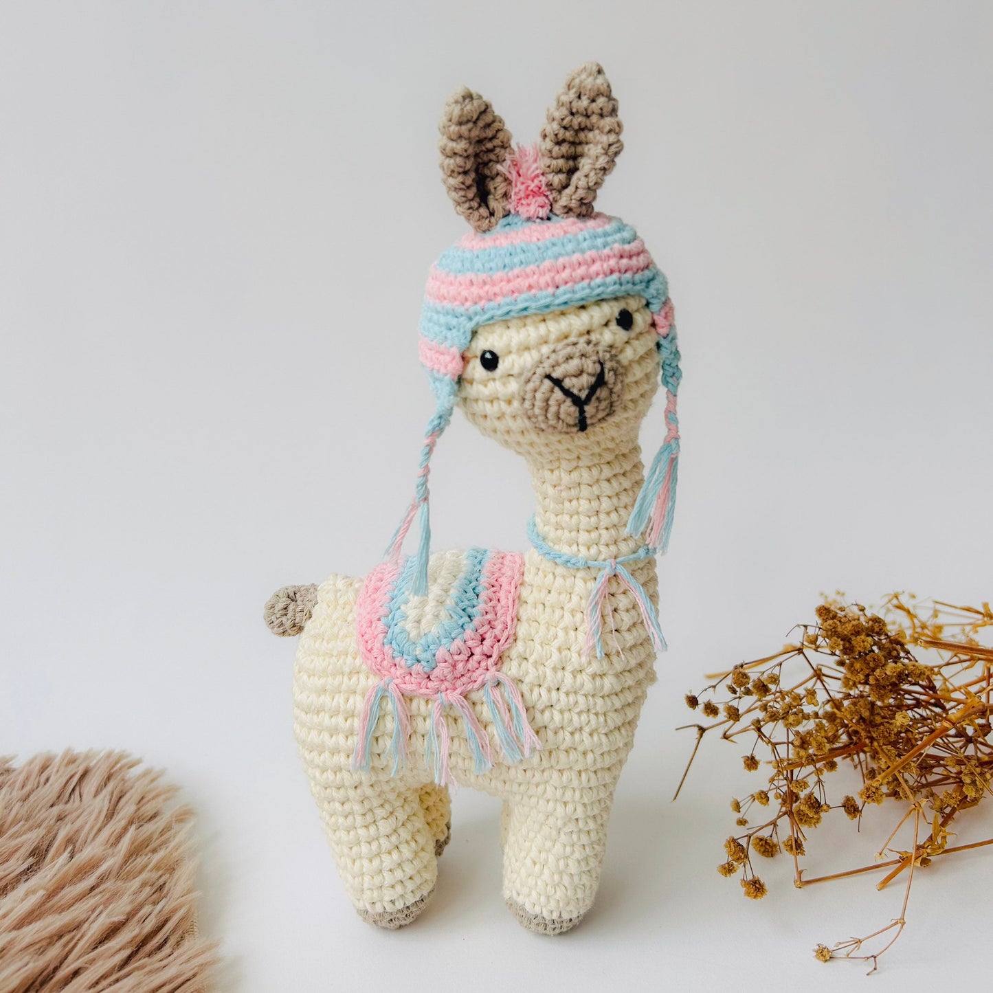 Crocheted llama toy wearing a colorful hat on a light background