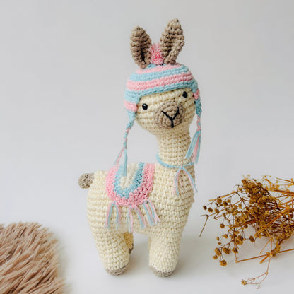 Crocheted llama toy wearing a colorful hat on a light background