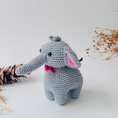 Crocheted elephant toy with a pink bow on a light background