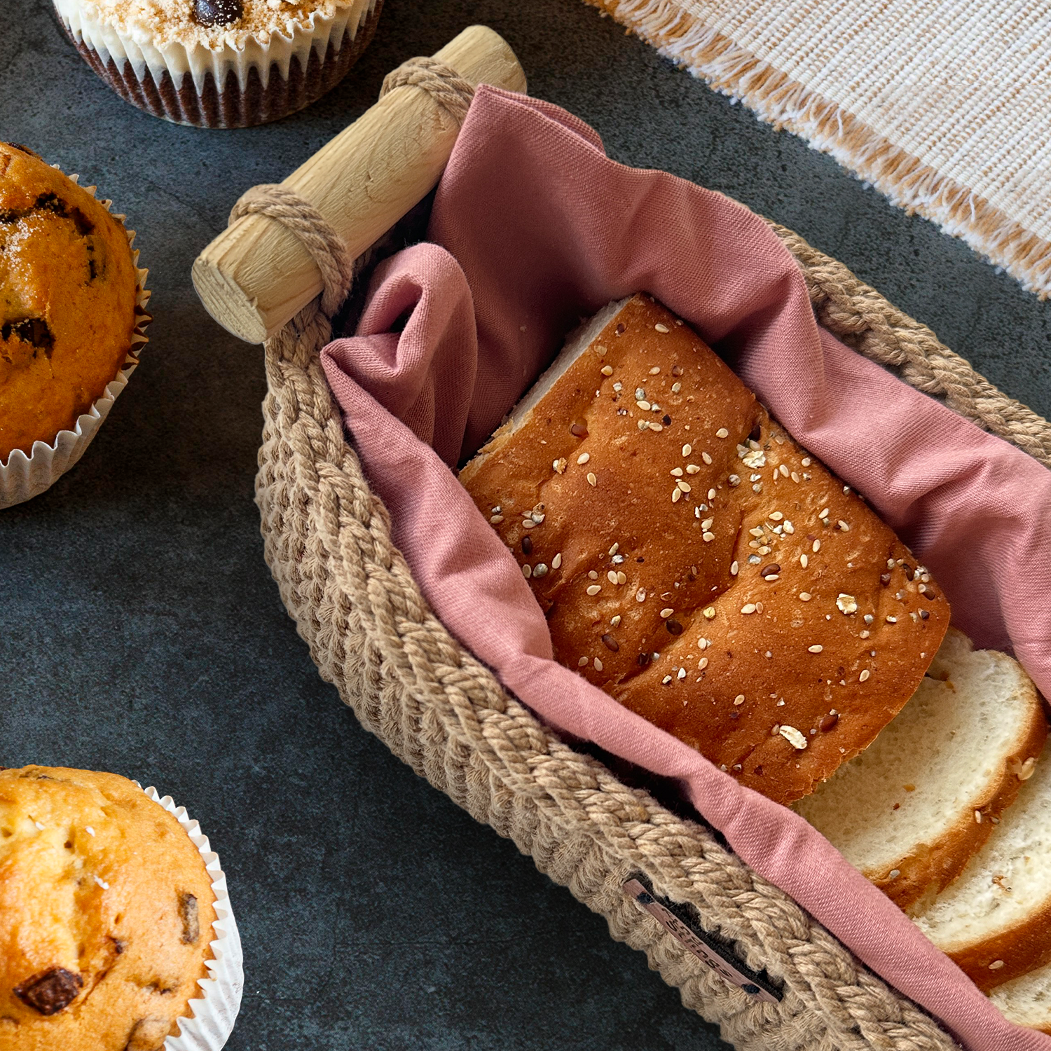 woven basket with pink cloth, surrounded by muffins on a dark surface.